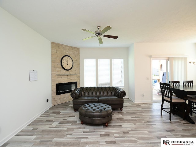 living area featuring a ceiling fan, wood finished floors, baseboards, and a stone fireplace