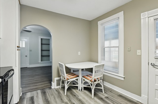 dining area with arched walkways, baseboards, and wood finished floors