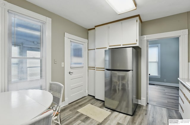 kitchen featuring freestanding refrigerator, light wood-style flooring, white cabinets, baseboards, and light countertops