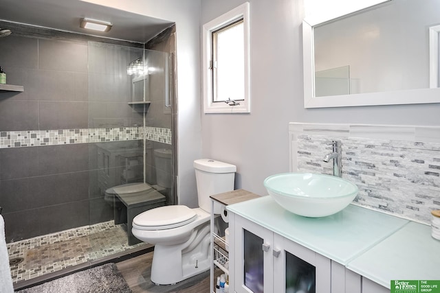 bathroom featuring toilet, a tile shower, wood finished floors, and vanity