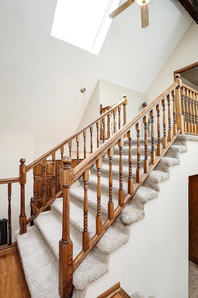 stairs featuring ceiling fan, wood finished floors, a skylight, and high vaulted ceiling