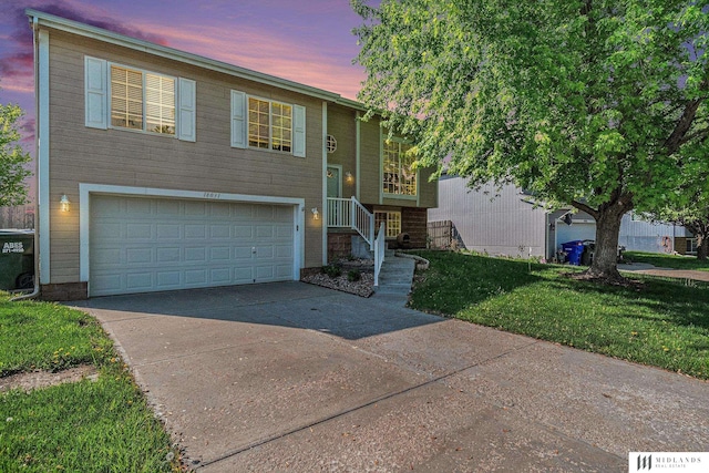 split foyer home featuring concrete driveway, an attached garage, and a yard