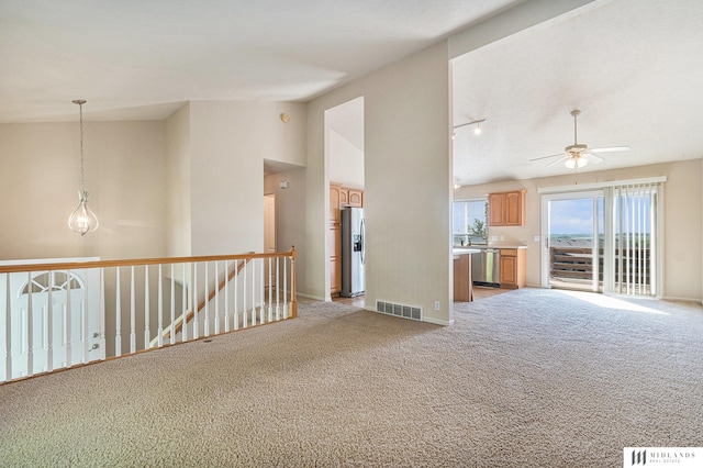 unfurnished living room with light colored carpet, ceiling fan, vaulted ceiling, and baseboards