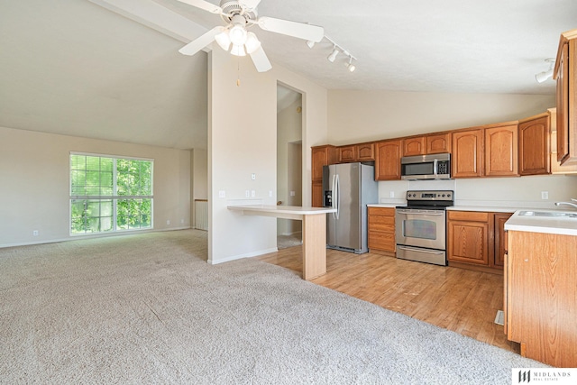 kitchen with appliances with stainless steel finishes, high vaulted ceiling, light colored carpet, track lighting, and brown cabinets