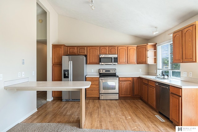 kitchen featuring appliances with stainless steel finishes, vaulted ceiling, a sink, brown cabinets, and light countertops