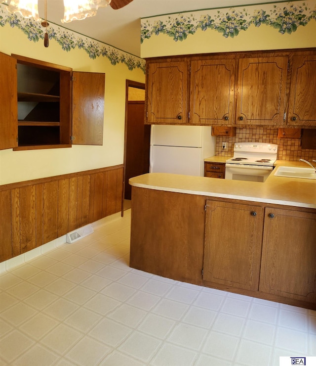 14930 Holmes St, Omaha, NE 68137 - kitchen with white appliances, a sink, a wainscoted wall, a peninsula, and light countertops
