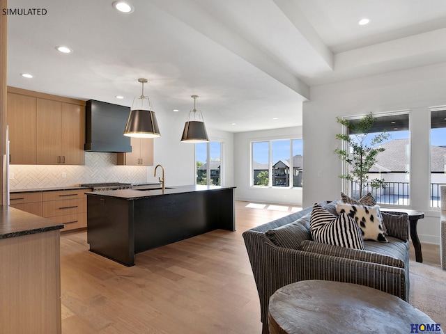 kitchen with wall chimney exhaust hood, a sink, backsplash, open floor plan, and light wood-type flooring
