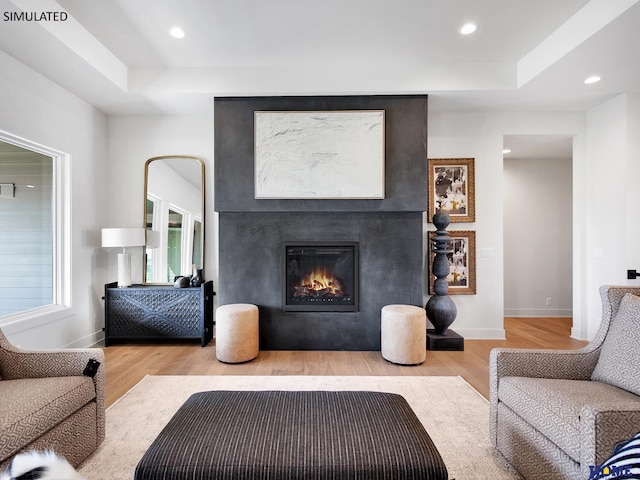 living area featuring wood finished floors, a tray ceiling, a large fireplace, baseboards, and recessed lighting