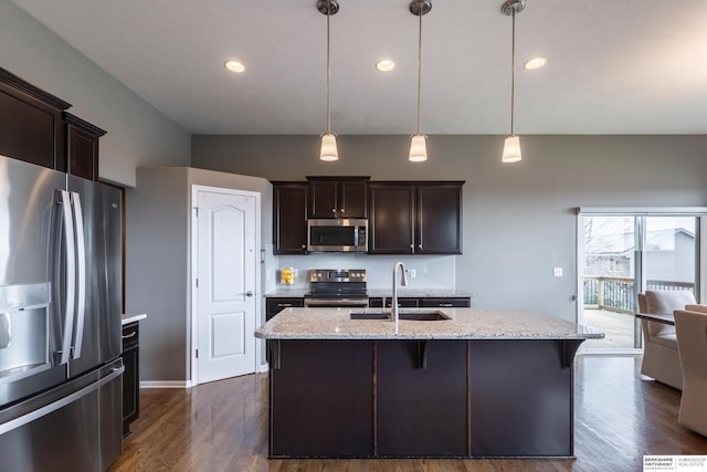 kitchen featuring appliances with stainless steel finishes, a sink, dark brown cabinetry, light stone countertops, and dark wood-type flooring
