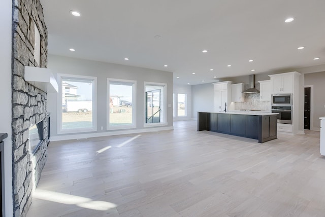 21108 Arlington St, Elkhorn, NE 68022 - kitchen with wall chimney range hood, stainless steel appliances, a stone fireplace, backsplash, and white cabinets