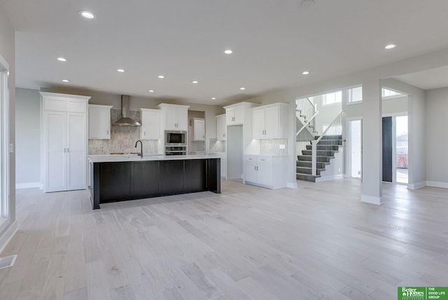 21108 Arlington St, Elkhorn, NE 68022 - kitchen featuring appliances with stainless steel finishes, wall chimney range hood, tasteful backsplash, white cabinetry, and light wood finished floors