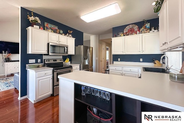 kitchen with stainless steel appliances, a sink, light countertops, white cabinets, and dark wood-style floors