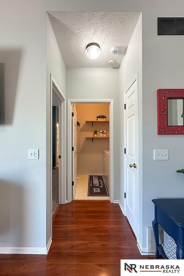 hallway featuring wood finished floors, baseboards, and a textured ceiling