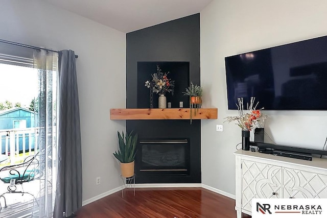 living area with wood finished floors, a glass covered fireplace, baseboards, and vaulted ceiling