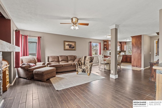 living room featuring a ceiling fan, dark wood-style floors, ornate columns, and baseboards
