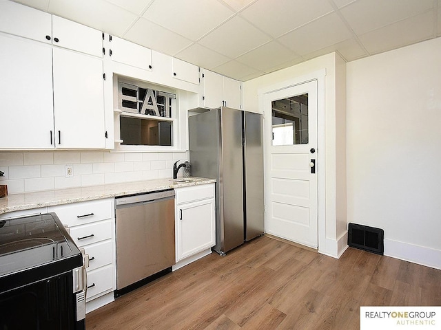 kitchen featuring appliances with stainless steel finishes, a paneled ceiling, white cabinetry, light wood-type flooring, and decorative backsplash
