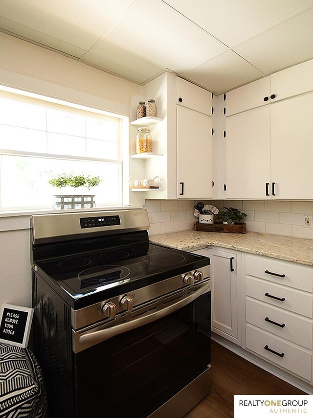 kitchen featuring stainless steel range with electric stovetop, backsplash, white cabinets, and light stone counters