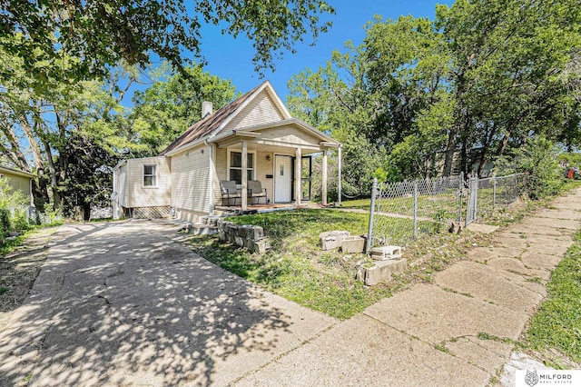 shotgun-style home featuring covered porch, concrete driveway, and fence