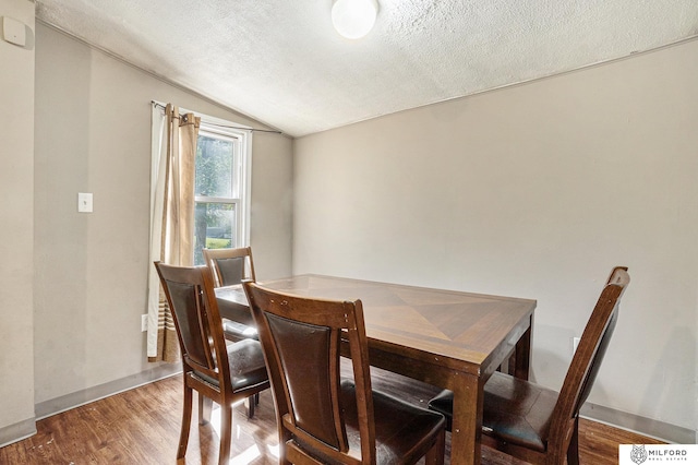 dining area with vaulted ceiling, a textured ceiling, wood finished floors, and baseboards
