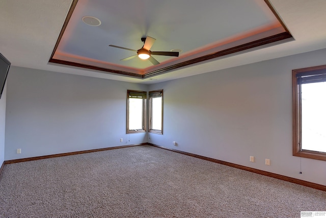 carpeted spare room with a tray ceiling, a ceiling fan, and baseboards