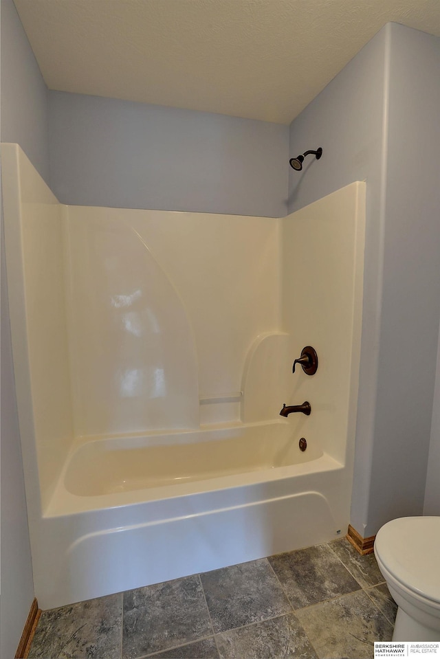 bathroom with baseboards, tub / shower combination, toilet, and stone finish floors