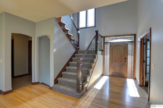 foyer entrance featuring arched walkways, wood finished floors, stairway, and baseboards