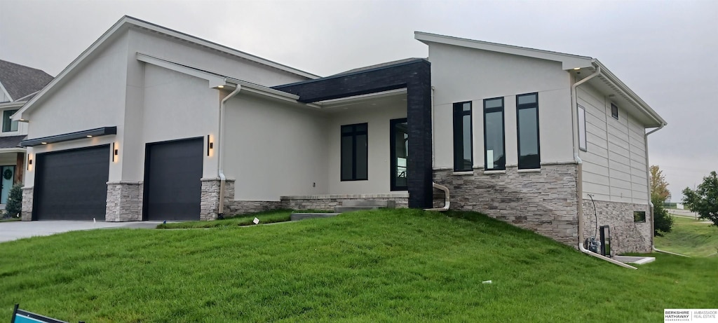 view of front of property with stone siding, an attached garage, a front yard, and stucco siding