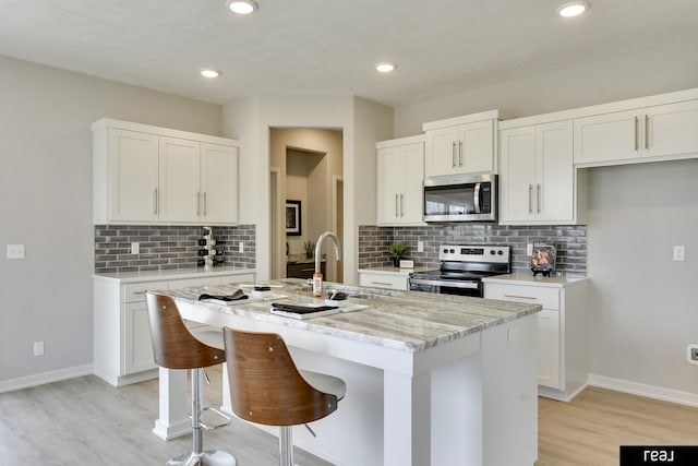 4406 Barksdale Dr, Bellevue, NE 68123 - kitchen featuring appliances with stainless steel finishes, light wood-style flooring, a sink, a center island with sink, and backsplash