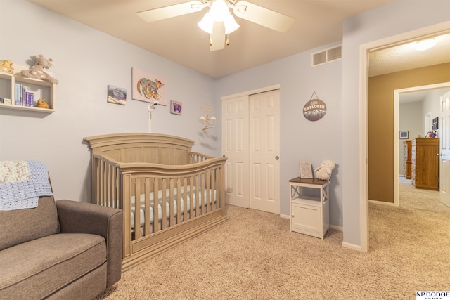 carpeted bedroom with a closet, a crib, a ceiling fan, and baseboards
