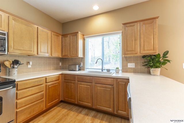 kitchen featuring a sink, range with electric cooktop, light countertops, light wood-style floors, and decorative backsplash