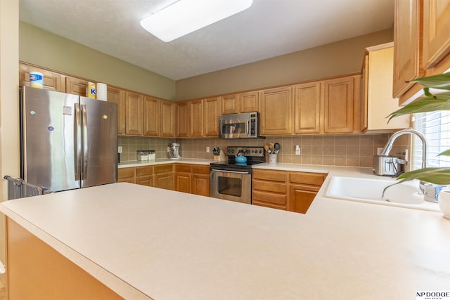 kitchen with appliances with stainless steel finishes, a sink, light countertops, tasteful backsplash, and a peninsula