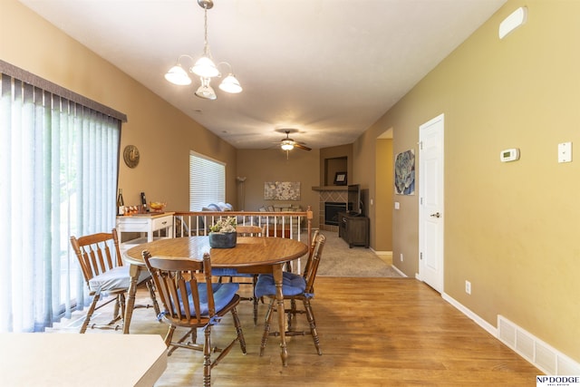 dining area with ceiling fan, a tiled fireplace, light wood-style floors, a chandelier, and baseboards
