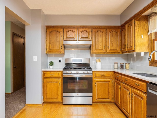 kitchen featuring stainless steel appliances, a sink, under cabinet range hood, and brown cabinets