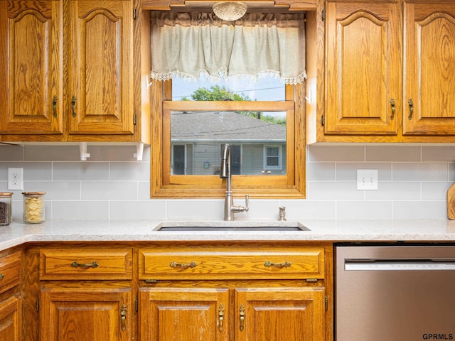 kitchen with dishwasher, a sink, tasteful backsplash, brown cabinetry, and light stone counters