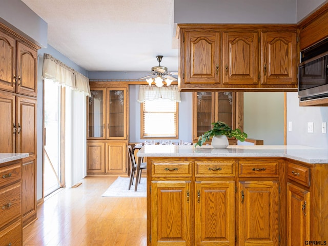 kitchen with brown cabinetry, light countertops, light wood-style flooring, a ceiling fan, and a peninsula