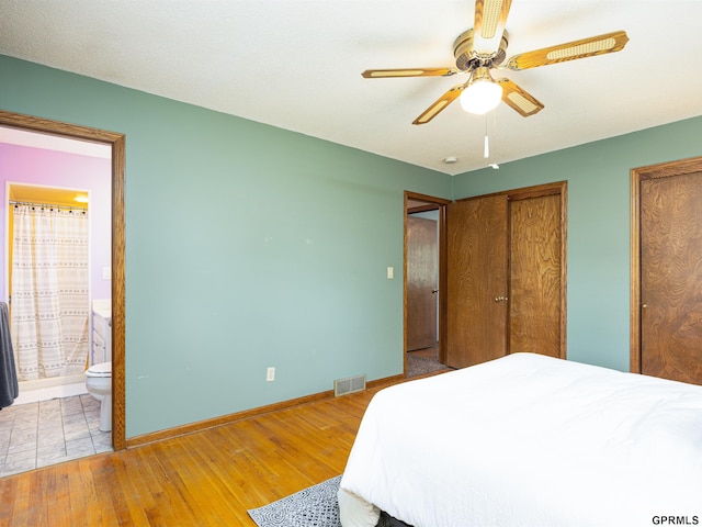 bedroom featuring wood-type flooring, two closets, baseboards, ensuite bath, and a ceiling fan