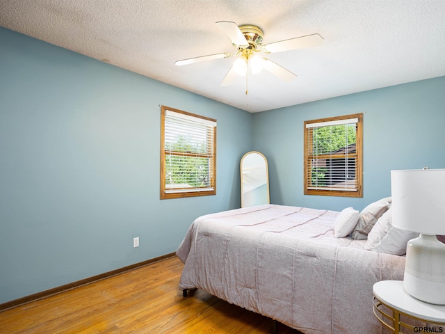 bedroom featuring wood finished floors, multiple windows, baseboards, a textured ceiling, and ceiling fan