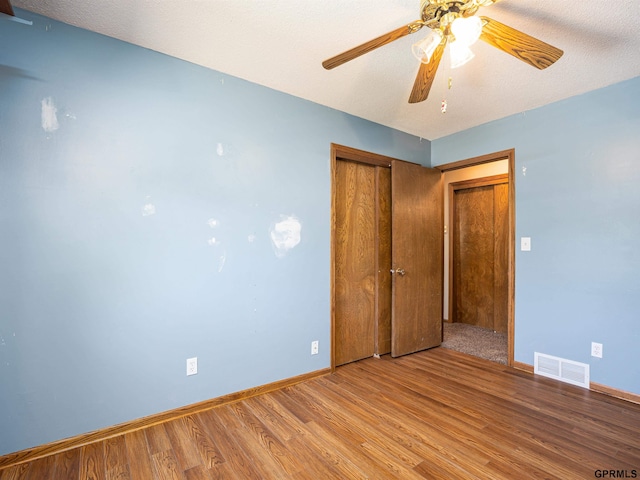 unfurnished bedroom with wood finished floors, baseboards, a closet, and a ceiling fan
