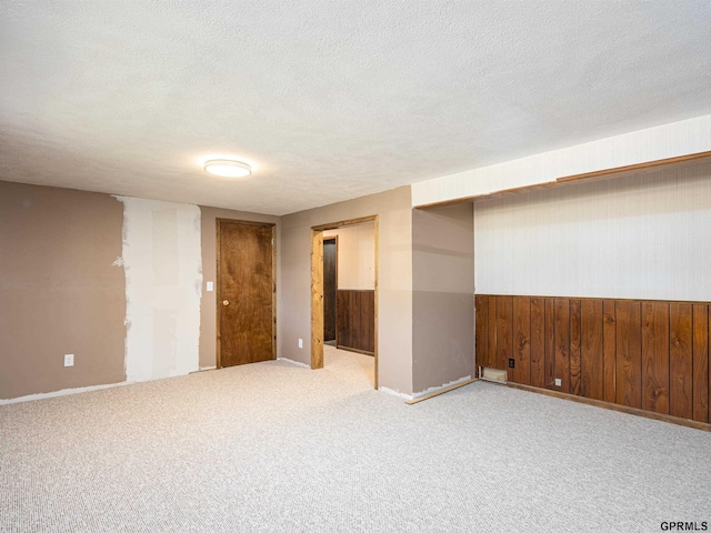 carpeted empty room featuring wood walls, a textured ceiling, and baseboards