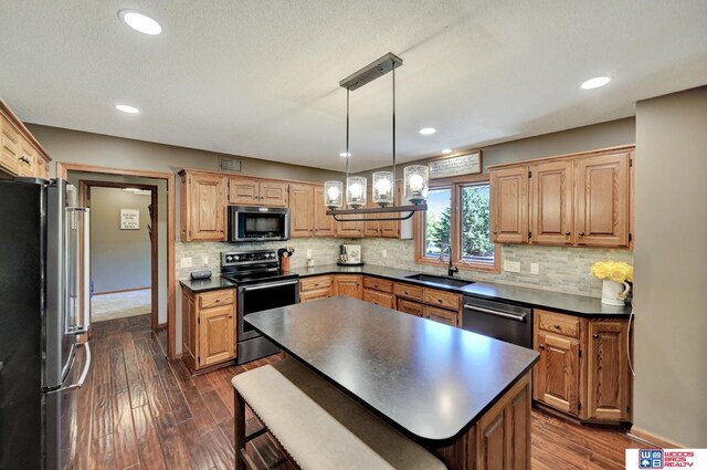 1714 S 14th Circle Dr, Beatrice, NE 68310 - kitchen featuring appliances with stainless steel finishes, a sink, dark countertops, dark wood-style floors, and a kitchen island