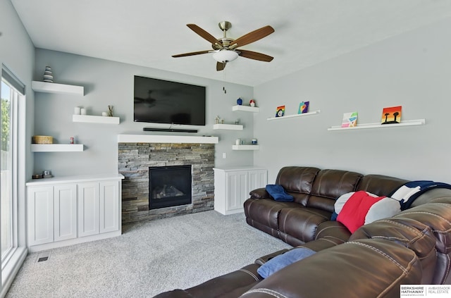 living room featuring carpet floors, ceiling fan, and a stone fireplace