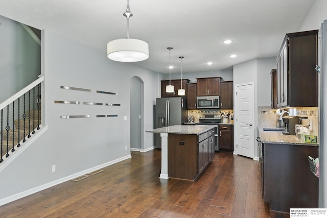 kitchen featuring appliances with stainless steel finishes, a sink, dark brown cabinetry, arched walkways, and a kitchen island