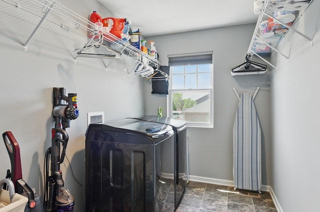 laundry room featuring washing machine and dryer, baseboards, and dark stone finish flooring