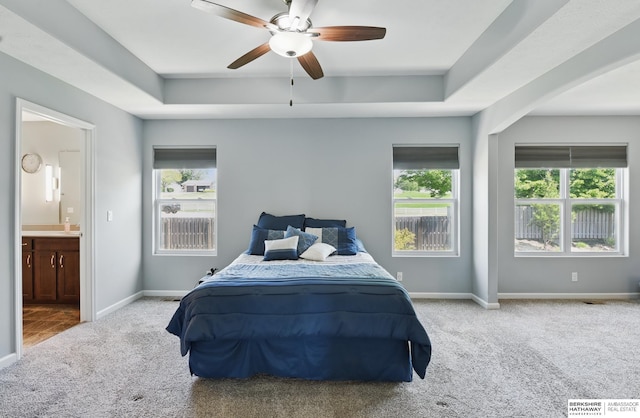 carpeted bedroom with multiple windows, a tray ceiling, ensuite bath, and baseboards