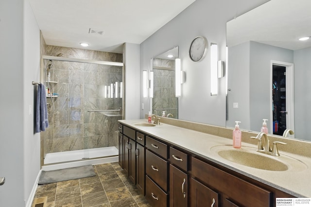 bathroom featuring a shower stall, double vanity, and baseboards