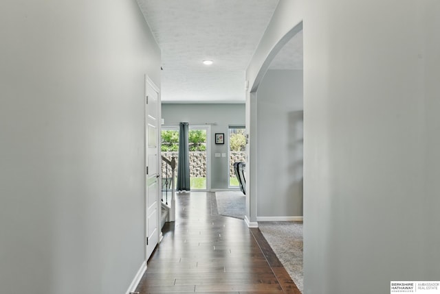 corridor featuring baseboards, arched walkways, dark wood finished floors, a textured ceiling, and recessed lighting