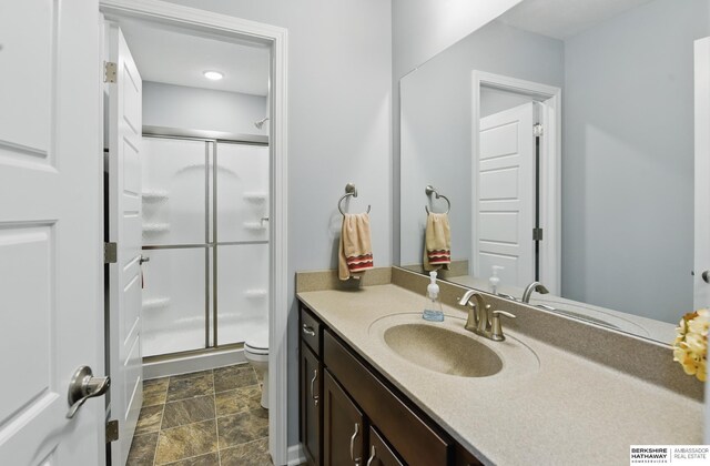 bathroom with a shower stall, toilet, stone finish floors, and vanity