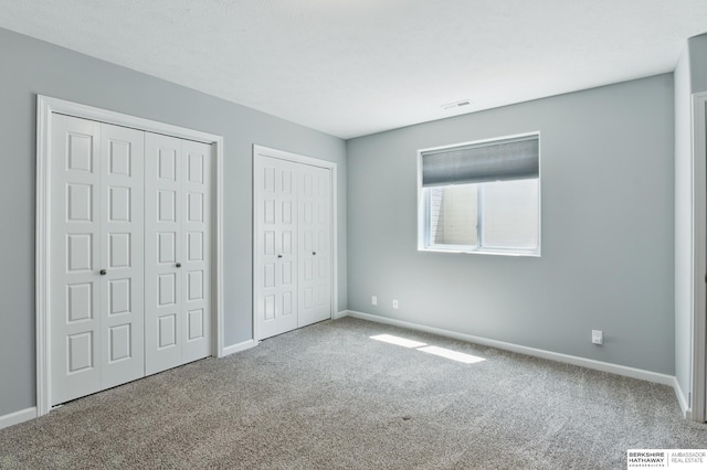 unfurnished bedroom featuring carpet flooring, two closets, and baseboards
