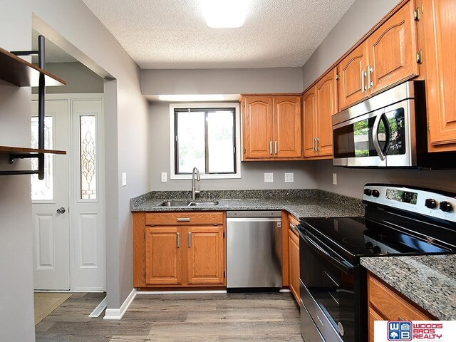 kitchen with appliances with stainless steel finishes, a sink, light wood finished floors, brown cabinets, and a textured ceiling