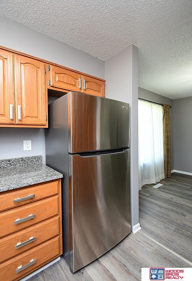 kitchen featuring freestanding refrigerator, light wood-style flooring, a textured ceiling, light stone counters, and baseboards
